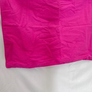 May include: A close-up of a vibrant fuchsia fabric, possibly a textile or garment. The material has a slightly wrinkled texture, with visible folds and creases. The color is a bright, saturated pink.