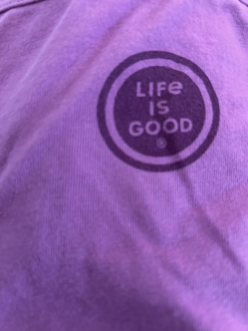 May include: Purple t-shirt with a white circle logo that says "Life is Good" in all caps.