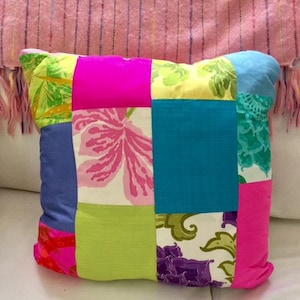 May include: A patchwork pillow with a variety of colorful fabrics, including pink, blue, green, yellow, and white. The pillow is made of squares of different fabrics sewn together.