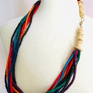 May include: Multi-strand necklace made of colorful wooden beads. The necklace features a long strand of beads in shades of red, orange, yellow, green, blue, purple, and black. The necklace is finished with a large wooden bead at the clasp.