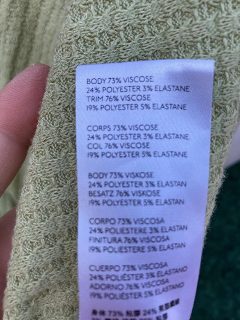 Puede incluir: Una etiqueta blanca con texto negro que detalla la composici&oacute;n de la tela de una prenda. La etiqueta indica que el cuerpo, el ribete, el cuerpo, el cuello, el adorno y la terminaci&oacute;n son 73% viscosa, 24% poli&eacute;ster y 3% elastano. El ribete, el cuello y el adorno son 76% viscosa, 19% poli&eacute;ster y 5% elastano. La etiqueta tambi&eacute;n incluye el texto "Cuerpo 73% Viscosa 24% poliester 3% elastano Adorno 76% Viscosa 19% poliester 5% elastano" y "身体73% 24% ₹整薬品".