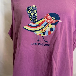 May include: Purple t-shirt with a colorful bird graphic and the text "Life is Good".