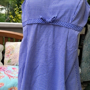 May include: Blue and white gingham print dress with spaghetti straps. The dress features a bow detail at the waist and a polka dot trim. The dress is displayed on a mannequin.