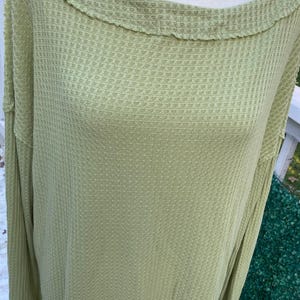 Puede incluir: Una blusa de manga larga de punto de waffle verde claro con cuello de barco.