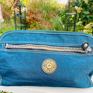 May include: A teal blue zippered travel makeup bag with a black and gold Kipling logo.