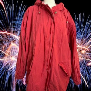 May include: A solid red hooded jacket featuring a front zipper closure, a high collar, and long sleeves with elasticized cuffs. The jacket includes two front pockets and a drawstring hood with metallic toggles, providing a functional outer layer.