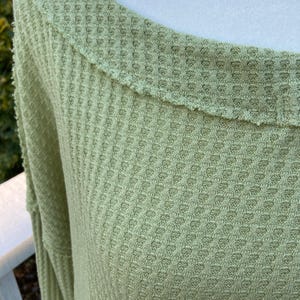 Puede incluir: Una camisa de manga larga de punto de waffle verde claro con un escote amplio y redondeado.