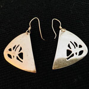 May include: A pair of silver earrings with a cut-out design in the shape of a leaf. The earrings are triangular and have a simple wire hook closure.