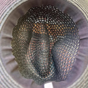 May include: A close-up of a sun hat, featuring a dark grey woven crown with small white and orange dots. The hat has a wide brim with a striped pattern in shades of grey and a dark grey interior.