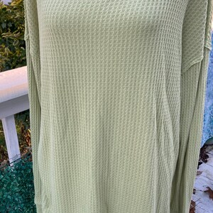 Puede incluir: Una blusa de manga larga de punto de waffle verde claro, de corte holgado y con un dobladillo ligeramente ca&iacute;do.