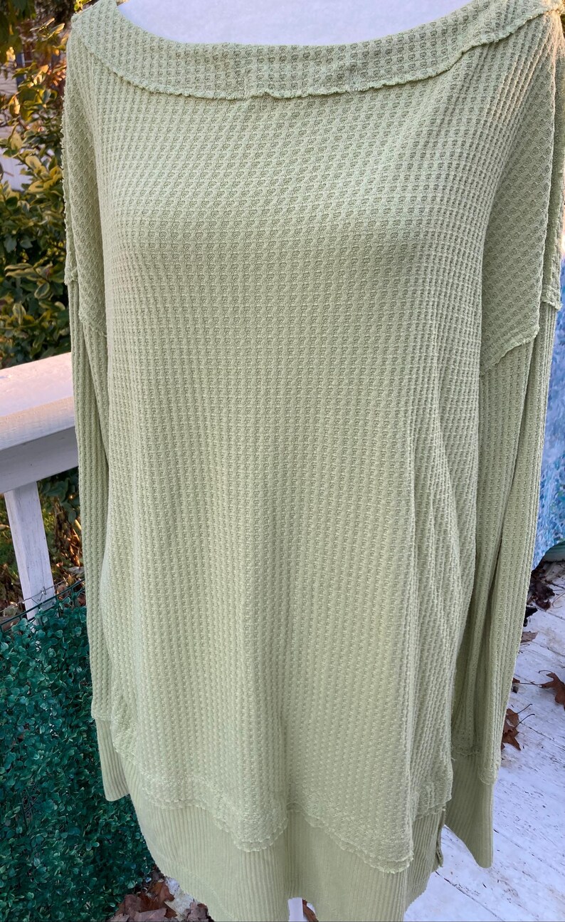 Puede incluir: Una blusa de manga larga de punto de waffle verde claro, de corte holgado y con un dobladillo ligeramente ca&iacute;do.