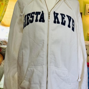 May include: White zip-up hoodie with a navy blue embroidered "SIESTA KEY" logo.