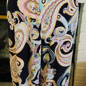 May include: Wide-leg pants with a paisley print in shades of pink, yellow, blue, and white on a black background.