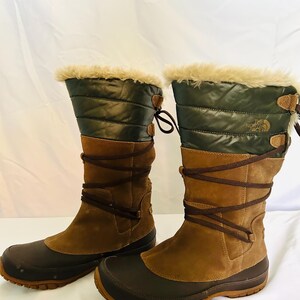May include: A pair of The North Face mid-calf boots featuring dark brown rubber toe caps, tan suede shafts, and dark olive green quilted nylon uppers. The boots have brown lace-up detailing and a beige faux fur trim along the top collar.