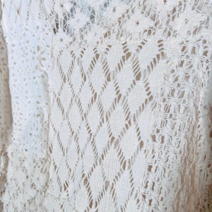 May include: Close-up of a cream-colored, open-weave fabric with a diamond and floral pattern. The fabric appears to be crocheted or knitted, with a delicate and airy texture. The design is intricate and detailed.