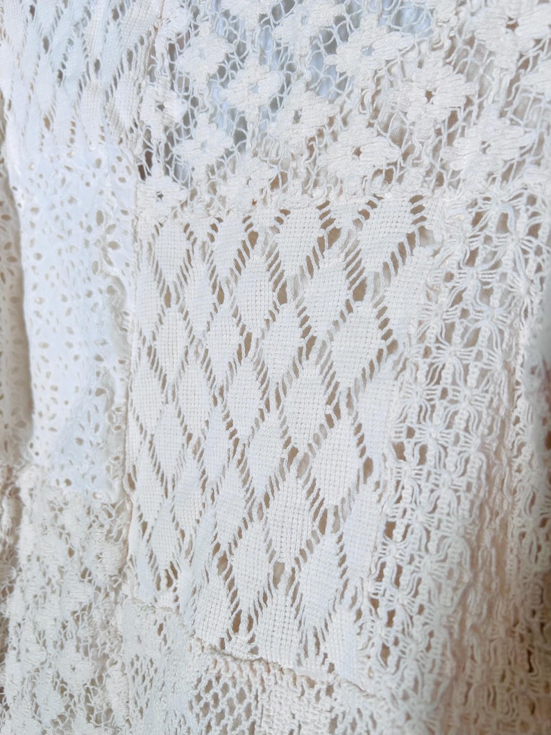 May include: Close-up of a cream-colored, open-weave fabric with a diamond and floral pattern. The fabric appears to be crocheted or knitted, with a delicate and airy texture. The design is intricate and detailed.