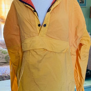 May include: A yellow and orange windbreaker jacket with a snap button closure and a zippered pocket. The jacket has a navy blue lining.