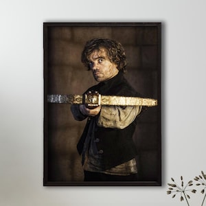 May include: A framed poster featuring a man with brown hair and a beard holding a crossbow. He is wearing a dark vest and a light-coloured shirt. The background is a dark brown brick wall.