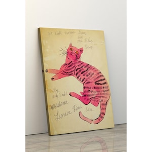Könnte beinhalten: Eine Illustration einer rosa Katze auf einer Leinwand. Die Katze liegt mit schwarzen Streifen und gelben Augen. Der Text auf der Leinwand lautet "25 Cats Name Sam and one Blue Pussy" und "By Andy Warhol Madame Leonor Fini Sam."