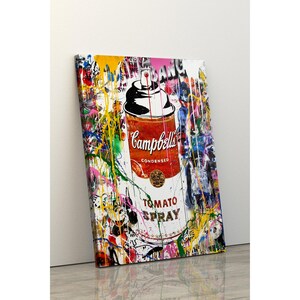 May include: A canvas print featuring a Campbell's Tomato Spray can design. The artwork is a vibrant mix of colors, with a red and white can as the central focus. Splattered paint and graffiti-style elements surround the can, creating a bold, pop art aesthetic.