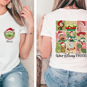 May include: White t-shirt featuring a Christmas-themed Alien character graphic on the front, with the name "Alexia" below. The back of the shirt displays a grid of Toy Story characters in Santa hats, with "Walt Disney World" text.