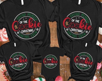 May include: Four black t-shirts with a Christmas cookie baking crew design. The shirts have the text "Proud Member of the Cookie Christmas Baking Crew" in a white circle with a gingerbread man and red and green cookies.