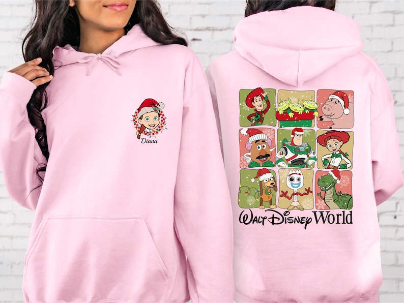 Puede incluir: Sudadera con capucha rosa claro. La parte delantera presenta un personaje de dibujos animados con un gorro de Pap&aacute; Noel y el nombre "Diana". La parte trasera muestra una cuadr&iacute;cula de personajes de Toy Story con gorros de Pap&aacute; Noel, con "Walt Disney World".