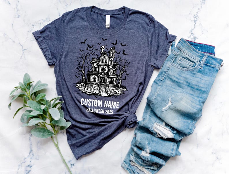 A dark blue t-shirt with a Halloween-themed graphic and the text "CUSTOM NAME HALLOWEEN 2015" printed on it, along with a pair of distressed blue jeans and some greenery.