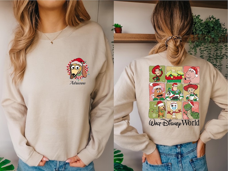 Puede incluir: Sudadera beige con un dibujo de Slinky Dog con un gorro de Pap&aacute; Noel y el nombre "Adrienne". La parte trasera tiene una cuadr&iacute;cula de personajes de Toy Story con gorros de Pap&aacute; Noel, con el texto "Walt Disney World".