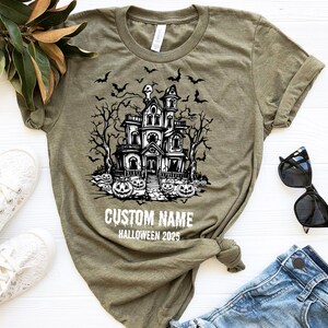 A t-shirt with a Halloween-themed graphic design, a pair of sunglasses, and some casual clothing items are arranged on a white surface.