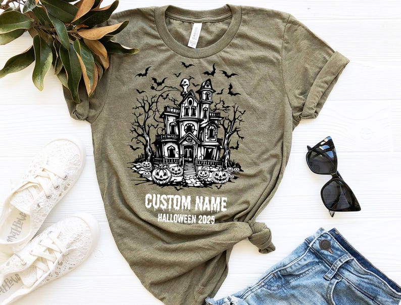 A t-shirt with a Halloween-themed graphic design, a pair of sunglasses, and some casual clothing items are arranged on a white surface.