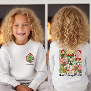 Puede incluir: Sudadera blanca con un dise&ntilde;o del Grinch con gorro de Pap&aacute; Noel y el nombre "Dominic" en la parte delantera. La parte trasera muestra una cuadr&iacute;cula de personajes de Toy Story con gorros de Pap&aacute; Noel y el texto "Walt Disney World".