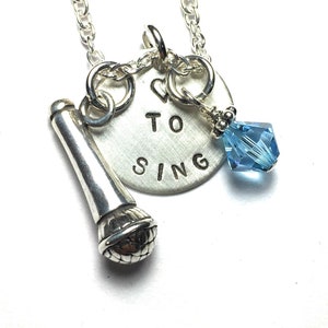 May include: Silver necklace with a microphone charm, a round charm with the text "I ♥ TO SING" and a light blue crystal charm.