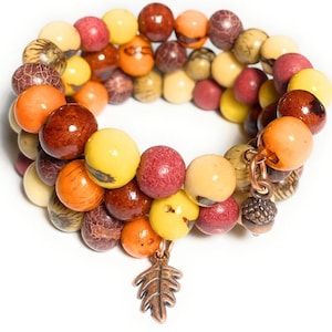 May include: A triple-strand bracelet made of wooden beads in shades of yellow, orange, red, and brown. The bracelet has a small copper leaf charm.