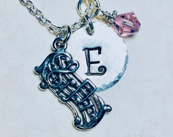 May include: A silver necklace with a music note charm, a silver charm with the letter E, and a pink crystal charm.