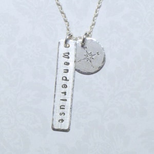 May include: Silver necklace with a compass charm and a bar charm that says "wanderlust".