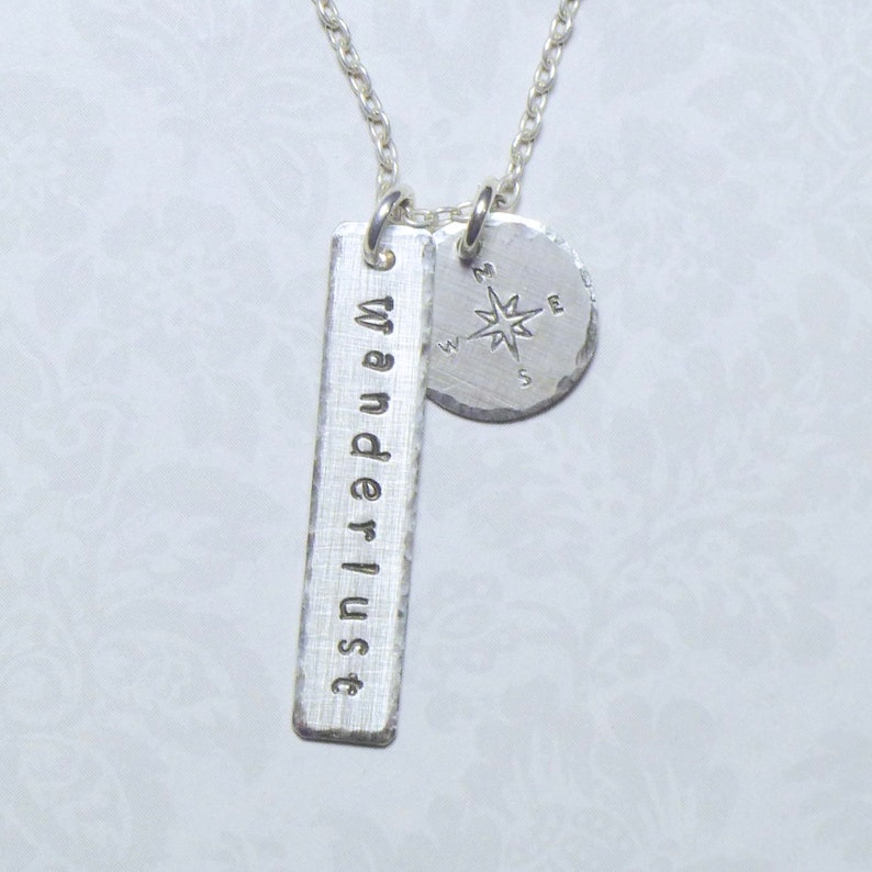 May include: Silver necklace with a compass charm and a bar charm that says "wanderlust".