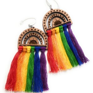 May include: Rainbow-colored tassel earrings with a wooden crescent moon and sun design. The earrings are made of wood and thread.