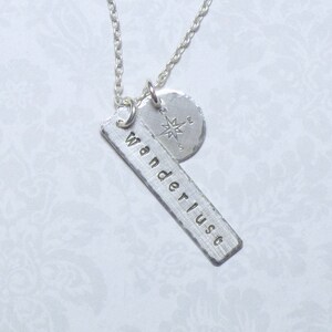 May include: Silver necklace with a compass charm and a rectangular tag that says "Wanderlust".