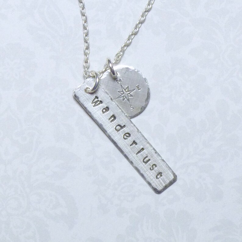May include: Silver necklace with a compass charm and a rectangular tag that says "Wanderlust".