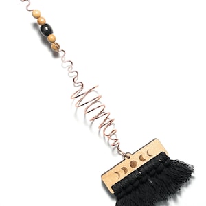 May include: A black tassel wall hanging with a wooden moon phase design. The hanging is attached to a copper wire with wooden beads.