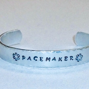 May include: Silver bracelet with a hammered finish. The bracelet has a star of life symbol and the text "PACEMAKER" engraved on it.