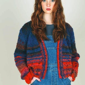 May include: A woman wearing a blue, red, and black patterned cardigan over a pair of blue denim overalls.