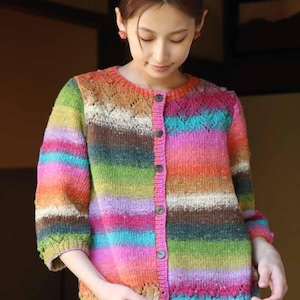 Puede incluir: Un cárdigan a rayas de colores con un frente abotonado y un delicado patrón de encaje en los hombros. El cárdigan está hecho de un hilo suave y texturizado y presenta una variedad de colores, incluyendo rosa, naranja, verde, azul y marrón.