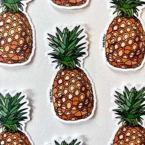 May include: A selection of pineapple stickers. Each sticker shows a detailed illustration of a pineapple with a textured, orange body and green leafy crown. The word "PINEAPPLE" is printed vertically on some stickers. The stickers are on a white background.