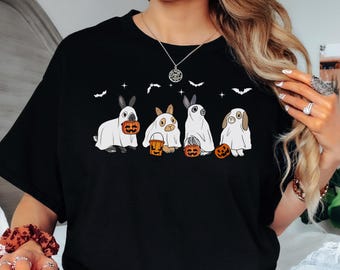 Könnte beinhalten: Schwarzes T-Shirt mit einem Halloween-Motiv. Das Design zeigt vier Cartoon-Hasen in Geisterkostümen, die jeweils einen Kürbis halten. Fledermäuse und Sterne sind ebenfalls Teil des Designs. Ein lässiges, festliches Kleidungsstück.
