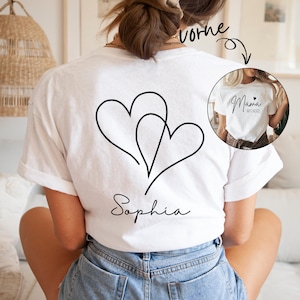 Op de afbeelding: Wit T-shirt met een zwarte omtrek van twee overlappende harten en de naam "Sophia" eronder gedrukt. Een kleinere afbeelding toont de voorkant van het shirt met de tekst "Mama mit Herz".