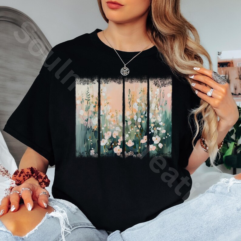 May include: Black t-shirt featuring a floral design. The design is divided into vertical panels with a watercolor-style illustration of flowers in shades of pink, green, and white. The background is a soft peach color.