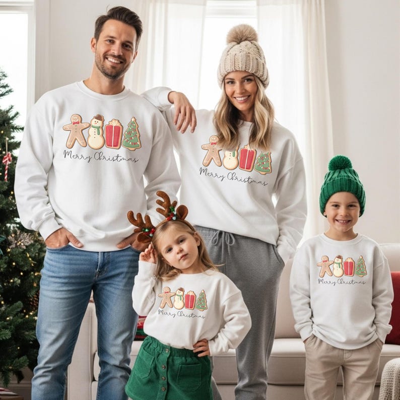 May include: White sweatshirts with a gingerbread man, snowman, gift, and Christmas tree design. The text "Merry Christmas" is below the graphic. The family is wearing matching sweatshirts. The little girl is wearing a green skirt and reindeer antlers.
