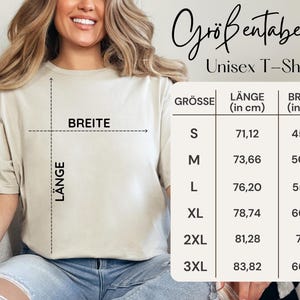 Puede incluir: Una camiseta unisex beige con una tabla de tallas. La tabla muestra las medidas en cent&iacute;metros de largo y ancho, desde la talla S hasta la 3XL. La camiseta se est&aacute; modelando.
